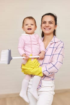 happy mother housewife is holding cute baby girl and doing housework at home , Happy family having fun