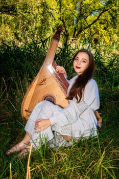 A girl with a musical instrument sits on the grass.