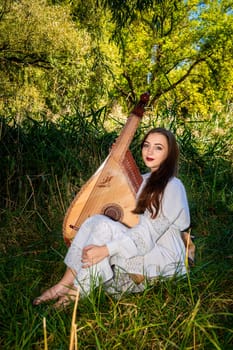 A female bandurist with a bandura is sitting on the grass in the park.