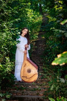 A young bandura player with a bandura stands on ancient stone steps in the park.