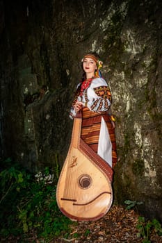 A bundoorist with a bandura is standing near a rock, dressed in Ukrainian national clothes