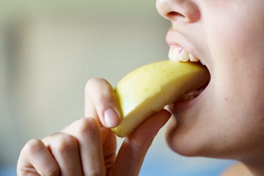 Closeup of crop unrecognizable teenage girl eating apple slice at home