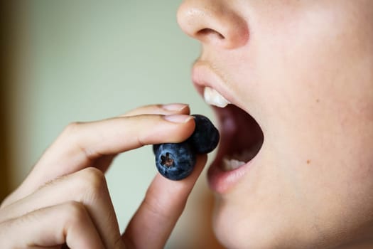 Closeup of crop anonymous young girl with mouth open about to eat delicious blueberries at home