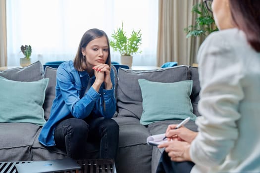 Sad young woman at therapy session with psychologist, psychiatrist. Therapist counselor and unhappy female patient on sofa in office. Psychology counseling treatment psychotherapy mental health youth
