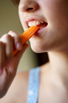 Closeup of crop anonymous young girl biting organic healthy carrot slice at home