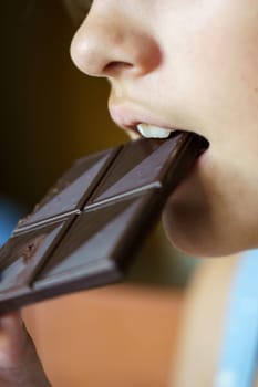 Crop anonymous young girl biting yummy chocolate bar at home
