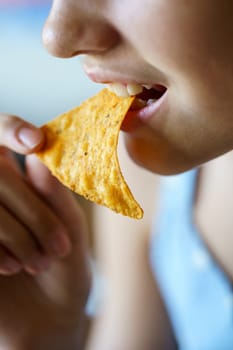 Closeup of crop anonymous teenage girl eating crunchy Mexican tortilla chip at home