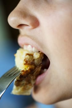 Closeup of crop unrecognizable teenage girl eating fresh delicious Spanish potato omelette from fork at home