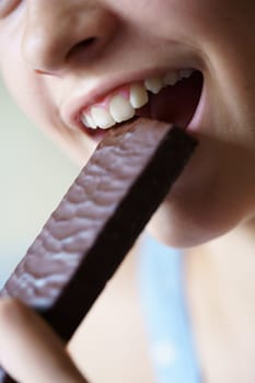 Closeup of crop anonymous teenage girl biting nutritious protein bar at home