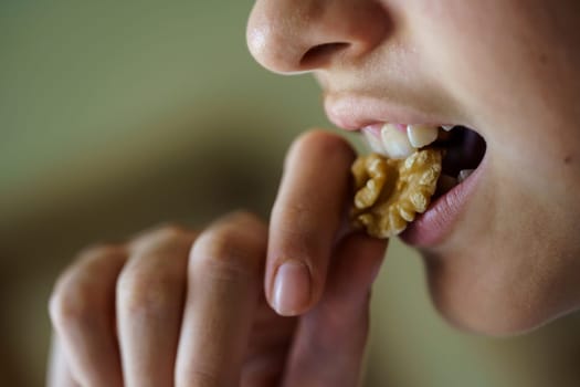 Side view of crop anonymous young girl eating fresh healthy walnut at home