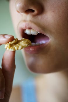 Closeup of crop anonymous teenage girl with mouth open about to eat delicious walnut at home