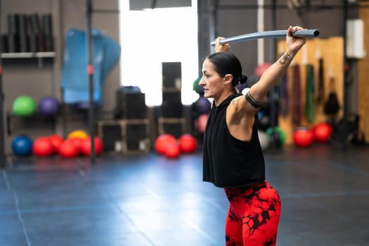 Horizontal photo with copy space of a mature woman warming up and stretching with a bar in a cross training gym