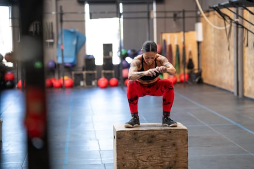 Strong fit woman squatting on a box in a gym after jump