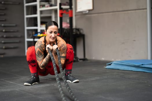 Strong woman squatting using a battle rope to work out in a gym