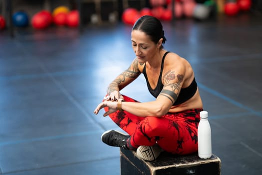 Sportswoman resting in the gym using smart watch sitting on a box