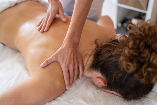 High angle of curly haired female getting back massage from professional osteopath during rehabilitation session in clinic