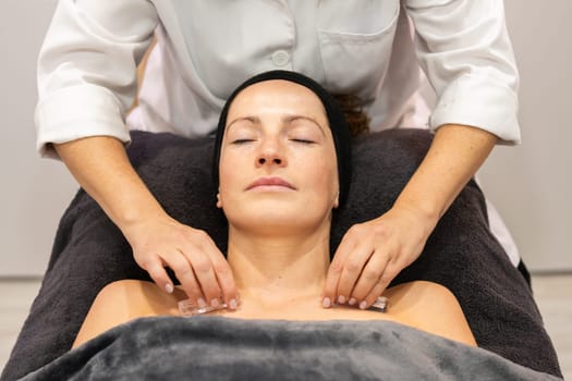 From above of crop anonymous beautician in uniform massaging body of female customer during beauty treatment at salon