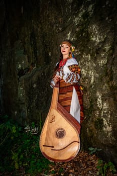 Ukrainian bandurist in national dress stands near a rock.