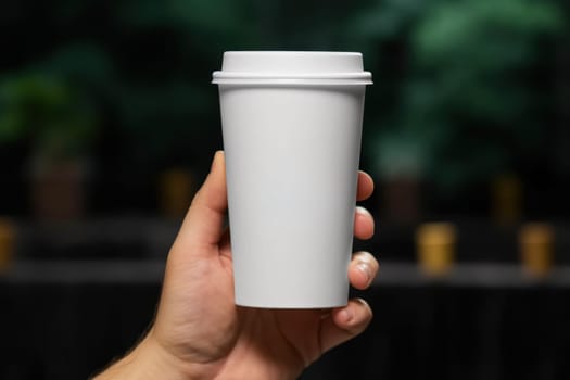Mock up of female hand holding blank coffee paper cup for advertising.