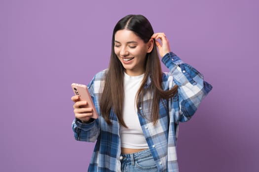 Young and enthusiastic woman scrolling music on her phone while putting her hair behind ear with attractive smile.