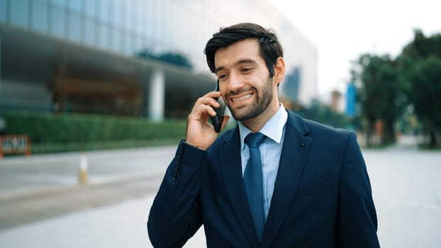 Skilled caucasian project manager calling phone while walking at city with blurred background. Skilled businessman using smart phone talking to project manager with blurred background. Exultant.