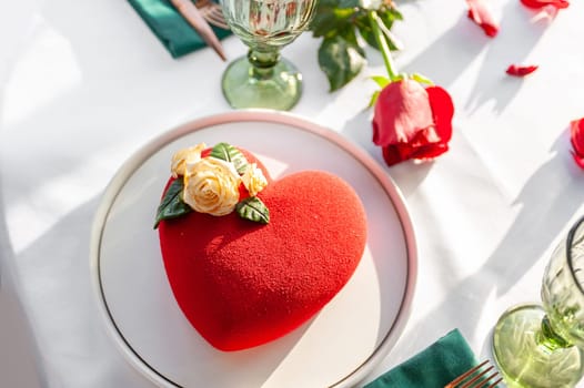 Heart Shaped Red Velvet Valentine's Day Cake on a white tablecloth with a red rose and rose petals in a restaurant. High quality photo