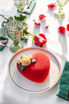 Heart Shaped Red Velvet Valentine's Day Cake on a white tablecloth with a red rose and rose petals in a restaurant. High quality photo