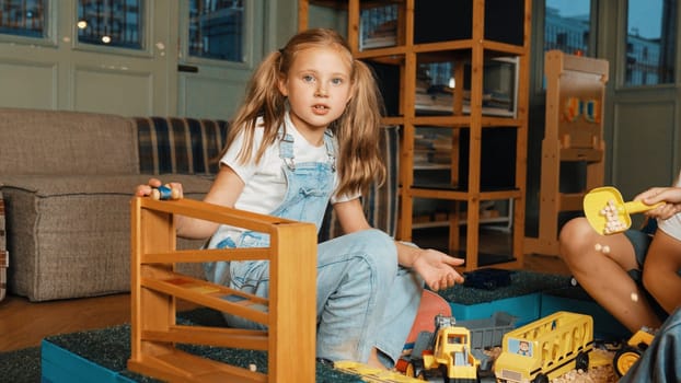 Happy smart girl playing car model while slide in rail at playroom. Cute caucasian student using wooden toy improve or develop creativity and imagination. Creative activity concept. Erudition.