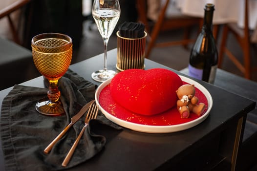 Heart Shaped Red Velvet Valentine's Day Cake with a bottle of sparkling wine and a glass in a restaurant. High quality photo