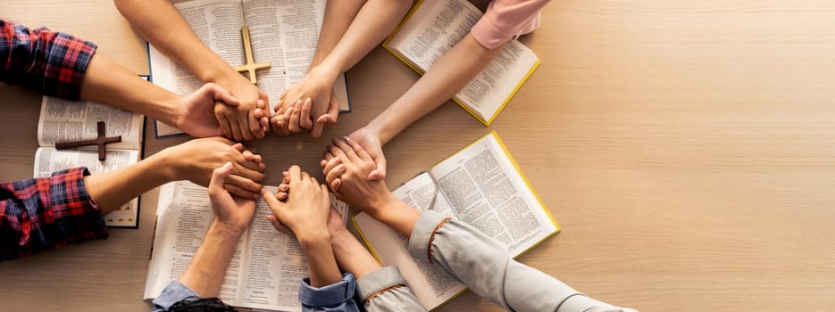 Cropped image of group of people praying together while holding hand on holy bible book at wooden church. Concept of hope, religion, faith, christianity and god blessing. Top view. Burgeoning.