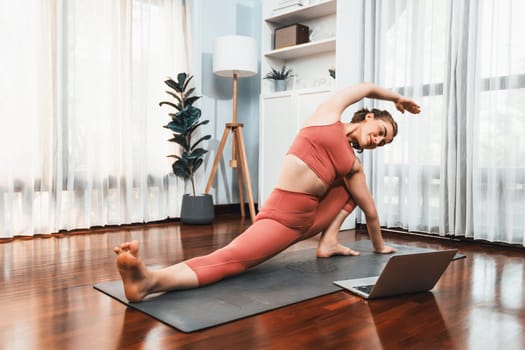 Flexible and dexterity woman in sportswear doing yoga position in meditation posture on exercising mat at home. Healthy gaiety home yoga online training session with peaceful mind and serenity.