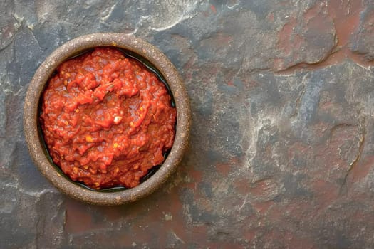 Harissa sauce, traditional in the Maghreb countries, made from hot red pepper, garlic and spices in a bowl on the surface of a natural stone.Top view.