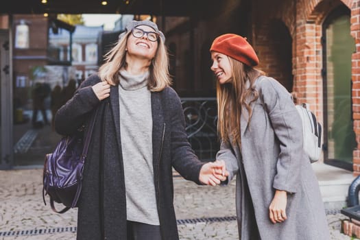 Young pretty girls friends having fun outdoor in autumn evening in city laughing and going crazy on the street - friendship and funny people