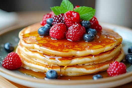 Pancakes with syrup, blueberries and raspberries on top on a table in a cafe.