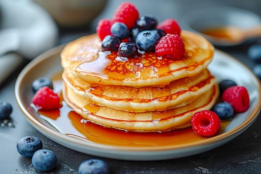 Pancakes with syrup, blueberries and raspberries on top on a table in a cafe.