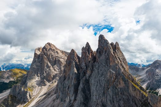 Bare peak and steep slopes of Seceda mountain range against cloudy sky. Observation deck overlooking giant ridgeline in Alps aerial view