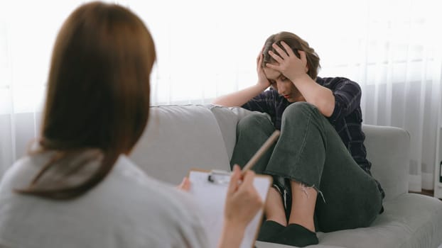 Sad PTSD woman patient in therapy for mental health with psychologist, depression or grief after life failure. Frustrated trauma young woman talking to prim psychologist about emotion in clinic