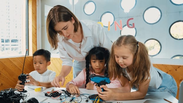 Teacher looking at children while diverse student looking at screen. Children excited in presentation while drawing or writing art books at table with toys and color pencil placed on table. Erudition.