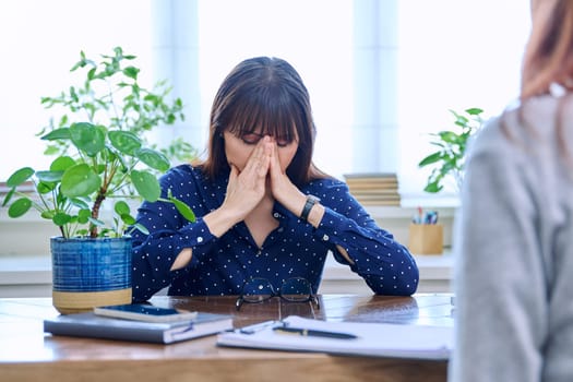 Mature sad woman in therapy session with mental professional psychologist, sitting at table in office of therapist counselor social worker. Psychology psychotherapy mental assistance treatment support