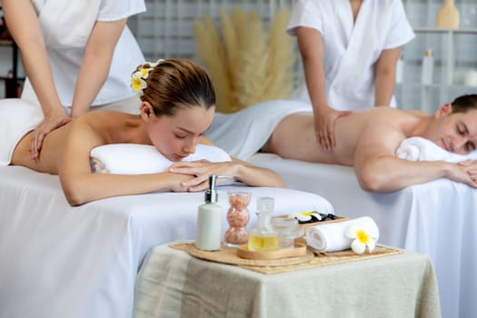 Caucasian couple customer enjoying relaxing anti-stress spa massage and pampering with beauty skin recreation leisure in day light ambient salon spa at luxury resort or hotel. Quiescent