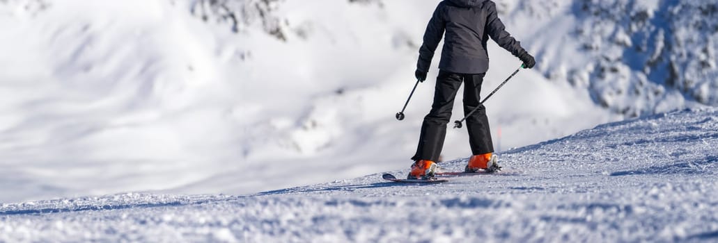 A skier, clad in a dark jacket and bright orange boots, carves a path on the glistening alpine slopes, with the snow-covered mountains offering a majestic backdrop. This moment captures the essence of winter sports—freedom and thrill in a frosty, serene world