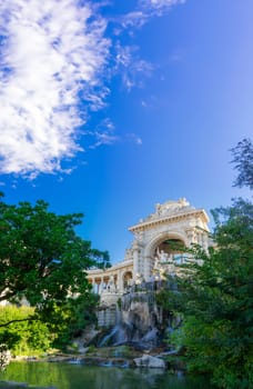 The Longchamp Palace stands grandly, its magnificent cascade and detailed stonework framed by lush foliage under a vibrant sky. This architectural marvel in Marseille harmonizes with nature, creating an oasis of history and beauty.