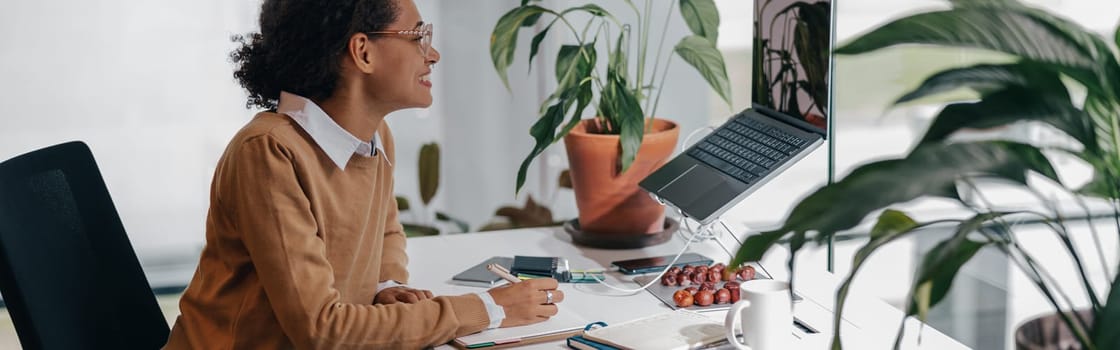 Female freelancer have video conference with client and making notes sitting in cozy coworking