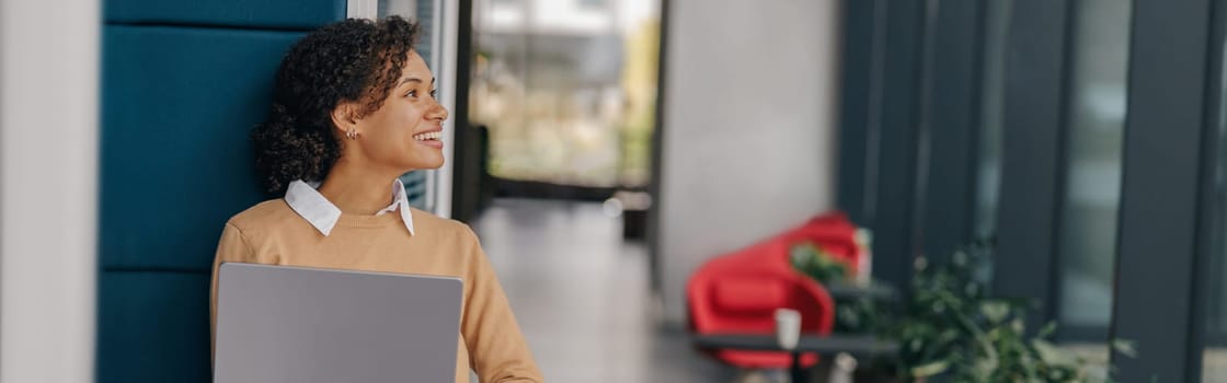 Young smiling business woman using laptop while standing on modern office background
