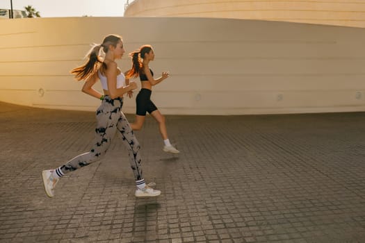 Two women athlete running side by side along an outdoor track on modern buildings background