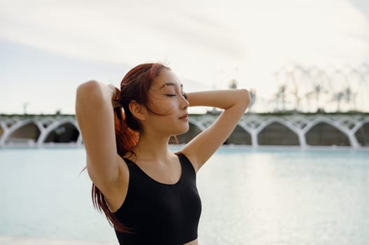 Female athlete in sportswear standing with raised arms and have a rest after morning jogging outside