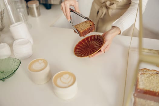 The waitress's hand puts the piece of cupcake on the table at a cafe standing behind bar counter