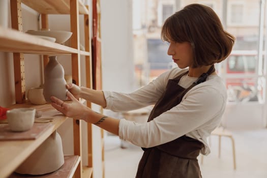 Young female potter holding unfired clay vase while standing in pottery studio. High quality photo