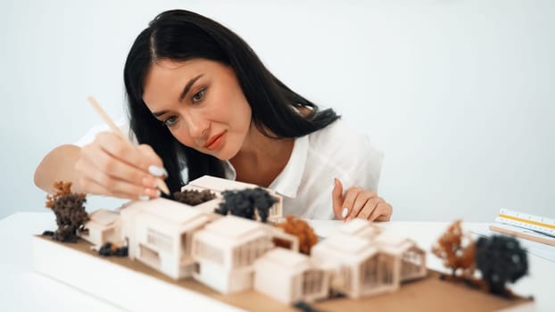 Closeup portrait image of young beautiful architect focus on measures the architectural model with blueprint placed on table in modern meeting room. Creative business design concept. Immaculate.