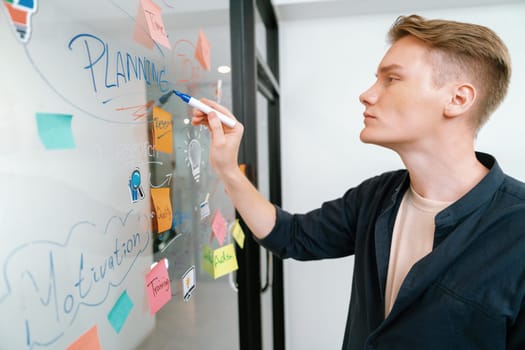 Professional caucasian male leader writing and sharing marketing idea by using mind map and sticky notes on glass board at modern meeting room. Creative business and planing concept. Immaculate.